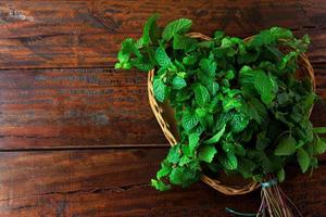 Group of green organic fresh mint in basket over rustic wooden desk. Aromatic peppermint with medicinal and culinary uses