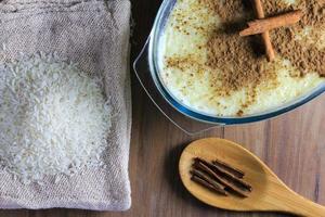 rice pudding with cinnamon in glass container on wooden table, rice over rustic bag