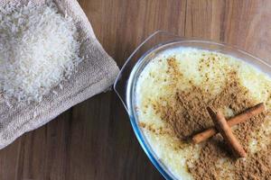 rice pudding with cinnamon in glass container on wooden table, rice over rustic bag