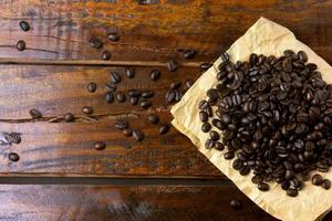 roasted coffee beans on paper on rustic wooden table, beans around scattered photo