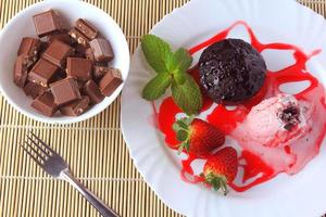 Petit Gateau con helado en un plato blanco con fresa sobre mesa de madera rústica foto