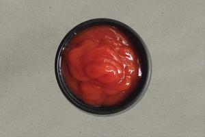 Close up view red delicious ketchup on black small plate laying on kitchen table. photo