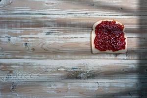 Slices of bread, sandwich with strawberry jam on old wooden table. photo