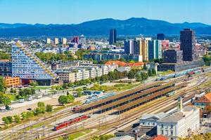 Aerial panorama of Ljubljana with modern buildings, the main train station, trains and beautiful green hills in the background, Slovenia photo