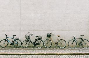 Four bicycles stand near a white brick wall. Several different bikes parked along an empty street in Copenhagen photo