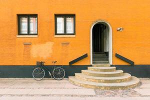 Bicicleta negra cerca de la pared de color amarillo anaranjado del antiguo edificio residencial en Copenhague, Dinamarca foto