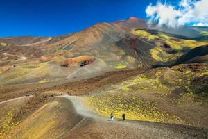 Beautiful valley landscape of The Mount Etna, Sicily, Italy. Colorful lava hills covered with plants and grass. People walking along the road between volcanic rocks and craters photo