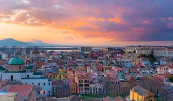 Sunset on Cagliari, panorama of the old city center with traditional colored houses, mountains and beautiful yellow-pink clouds in the sky, Sardinia Island, Italy