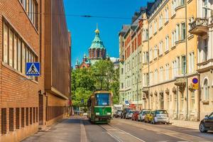 A street of Helsinki with an old style tram, parked cars, colorful historical buildings and the Uspenski Cathedral, Finland