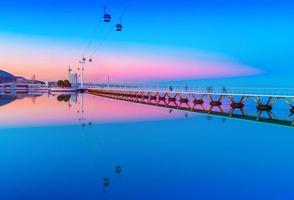 pintoresca puesta de sol sobre el parque de las naciones en lisboa, portugal. Paisaje nocturno con la carretera del teleférico y el puente reflejado en el agua foto