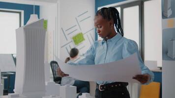 Woman architect analyzing building model and blueprints plans for project development video