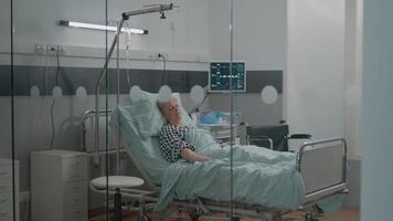Krankenschwester, die den schlafenden alten Patienten im Bett überprüft