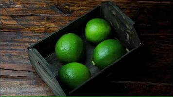 Limones frescos cosechados en la plantación y colocados en una caja sobre una mesa de madera