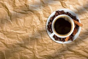 Top view of a cup coffee, with coffee beans and cinnamon sticks isolated on bread paper.
