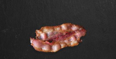 crispy thick cut smoked bacon slices isolated on dark background, close up view suitable for food design project. photo