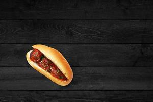 Close up view of tomatoes hotdog isolated on black wooden table. photo