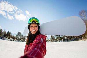 Beautiful young woman with the snowboard making selfie photo