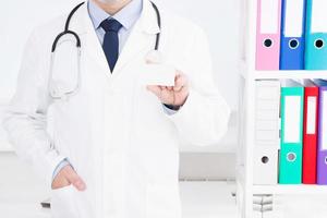 Doctor showing business card in clinic, medical insurance, man in white uniform. Copy space photo