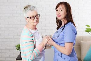 Happy senior woman holding hand nurse in home or clinic photo