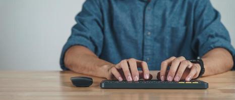 Cerca de las manos del hombre escribiendo en el teclado de la computadora en la mesa de madera en la oficina en casa o en el lugar de trabajo. foto