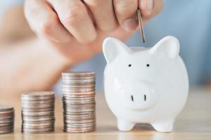Closeup of man hand putting money coin into piggy bank for saving money. saving money and financial concept