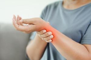 Closeup of woman sitting on sofa holds her wrist, hand injury with red highlight, feeling pain. Health care and medical concept. photo