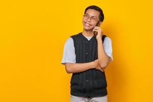 Retrato de feliz apuesto hombre asiático hablando por teléfono móvil sobre fondo amarillo foto