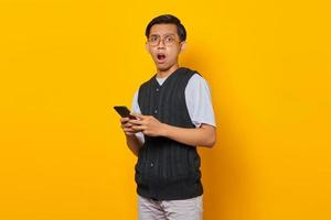 Portrait of a surprised handsome young man using smartphone on yellow background photo