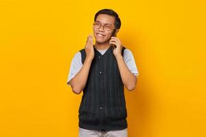 Retrato de hombre asiático guapo emocionado hablando por teléfono móvil sobre fondo amarillo foto