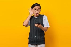 Retrato de hombre asiático de aspecto serio tratando de escuchar una conversación secreta y sosteniendo el teléfono inteligente foto