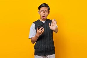 Surprised Asian young man with open mouth holding smartphone and doing stop motion with palms photo