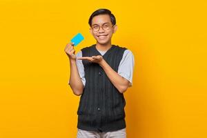 Cheerful asian man showing blank card with palm isolated on yellow background photo