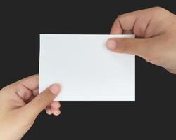 a close up of two hands holding a blank white paper. showing a virtual business card template on the black background. photo