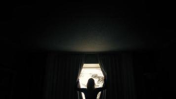 Femme ouvrant des rideaux avec un soleil éclatant derrière video