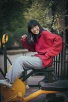 Adolescente asiático gracioso rostro riendo sentado en el equipo de ejercicio del parque foto