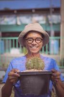 asian man raising melocactus pot and toothy smiling with happiness photo