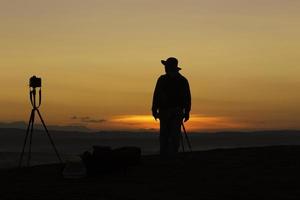 Fotógrafo de silueta parado solo y la cámara dispara durante el amanecer en bueng kan hin sam wan tailandia. foto