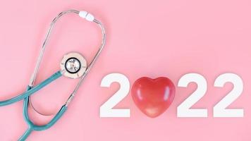 chequeo médico y seguro de salud en concepto de año 2022, estetoscopio con texto año nuevo 2022 sobre fondo rosa aislante. calendario de citas médicas para el examen médico anual 2022. atención médica foto