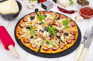 Tasty pizza with salami, mozzarella, mushrooms and olives on wooden background. photo