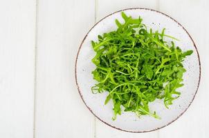 Vegetarian food. Fresh green arugula on plate, white wooden background. photo