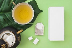 overhead view herbal tea cup with sugar cubes tea bag box green background