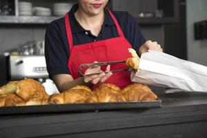 close up female baker putting croissant paper bag photo