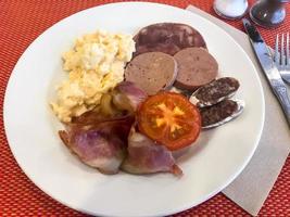 Set of dishes on breakfast table. Scrambled eggs, omelette, pate, croissants, champignons, crispy bacon, sausages. photo