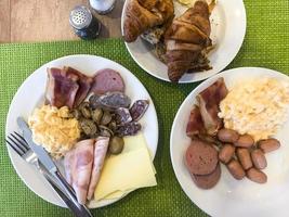 Set of dishes on breakfast table. Scrambled eggs, omelette, pate, croissants, champignons, crispy bacon, sausages. photo