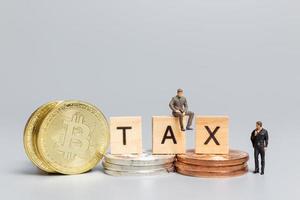 Miniature people, Businessman with Crypto Currency and wooden letters TAX photo