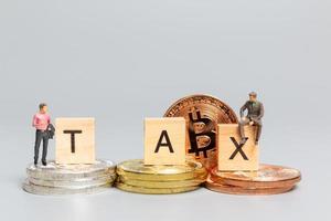 Miniature people, Businessman with Crypto Currency and wooden letters TAX photo