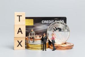 Miniature people, Businessman with Crypto Currency and wooden letters TAX photo