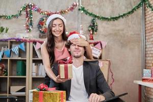 Sorprenda al equipo de dos compañeros de trabajo y al jefe dando regalos mientras el negocio trabaja antes de las vacaciones de la empresa en el lugar de trabajo de la oficina, está decorado para la celebración del festival de Navidad y la fiesta de año nuevo. foto