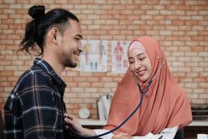 médico joven y bella mujer está examinando la salud del paciente masculino en la oficina de la clínica del hospital y asesorando con una sonrisa sobre los medicamentos. este especialista médico asiático es una persona islámica que lleva un hiyab. foto