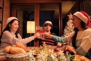 Happiness family and friends are celebrating, raising glasses and a cheerful smile with drinks, enjoy eating foods in home's dining room, decorated for Christmas festival party and New Year's Day. photo